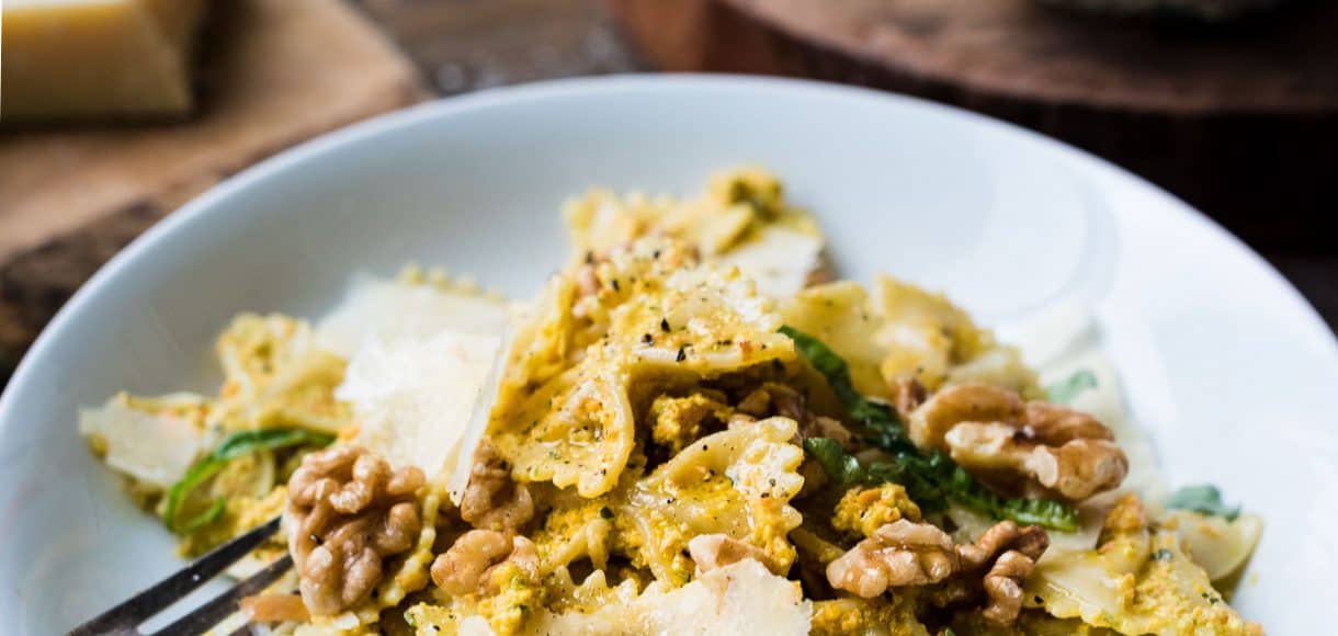 Farfalle with Roasted Carrot Pesto garnished with toasted walnuts and Parmesan cheese on a white plate.