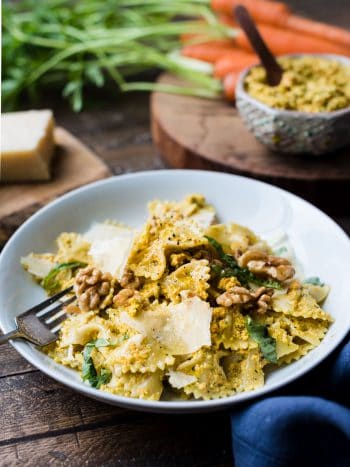 Farfalle with Roasted Carrot Pesto garnished with toasted walnuts and Parmesan cheese on a white plate.