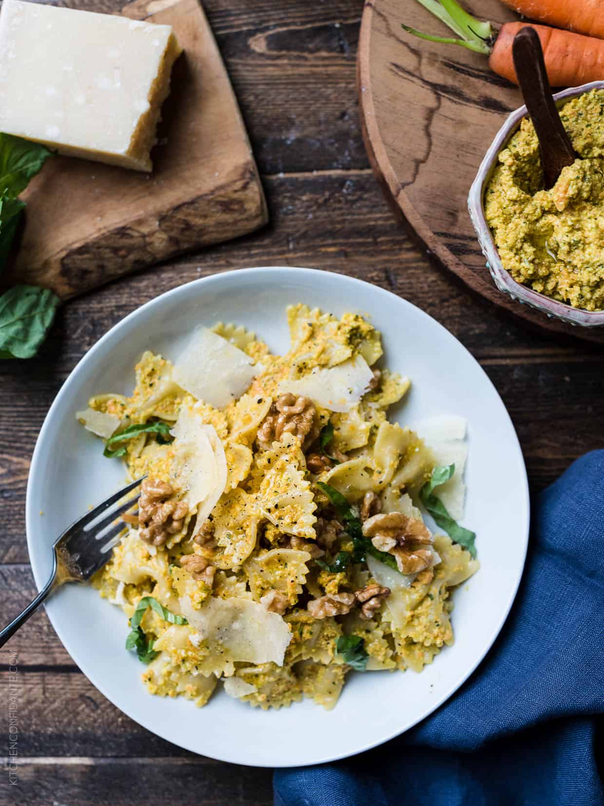 Farfalle with Roasted Carrot Pesto garnished with toasted walnuts and Parmesan cheese on a white plate.