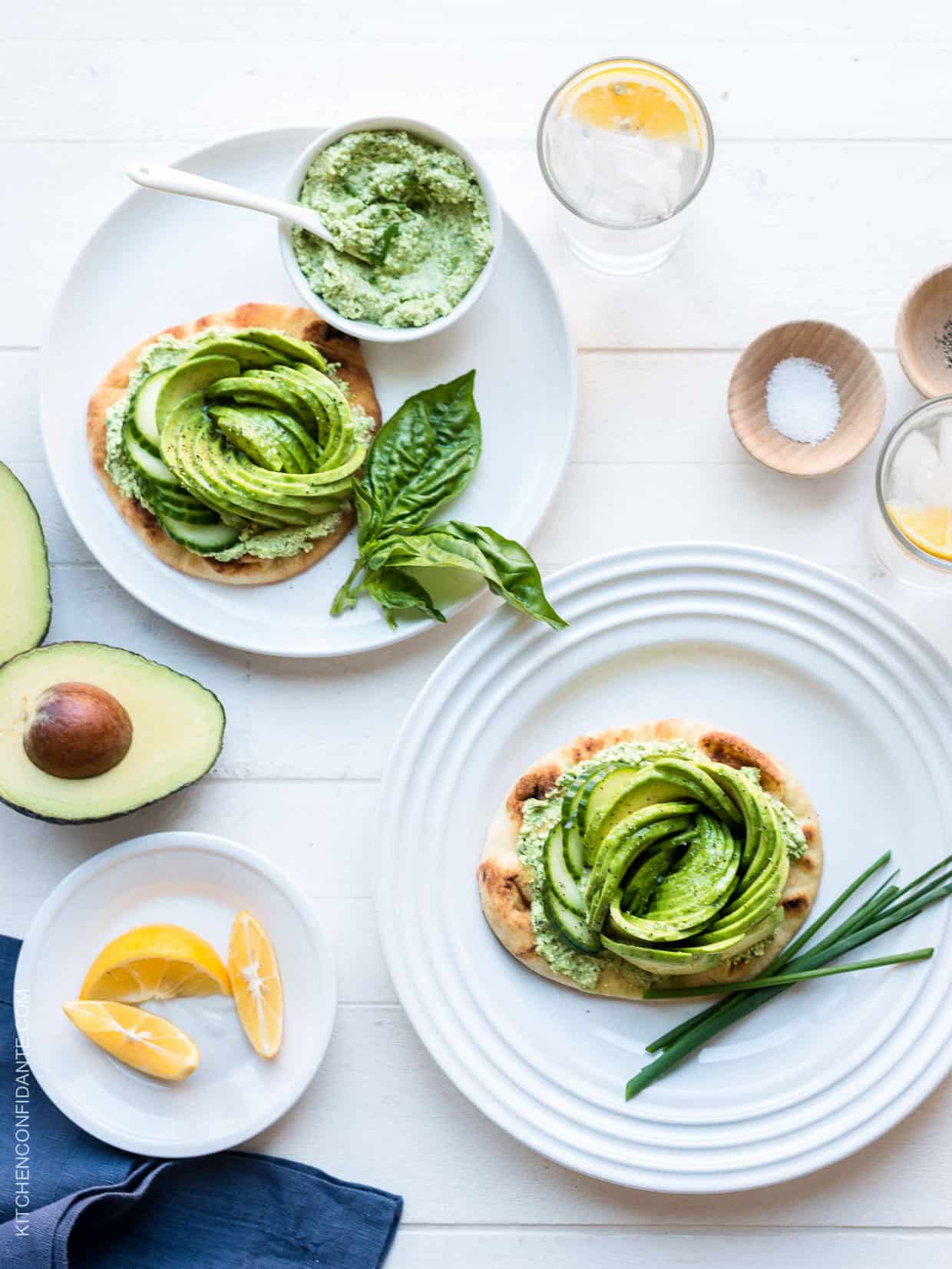 Toasted naan topped with Green Goddess feta spread and an avocado rose served on white plates.