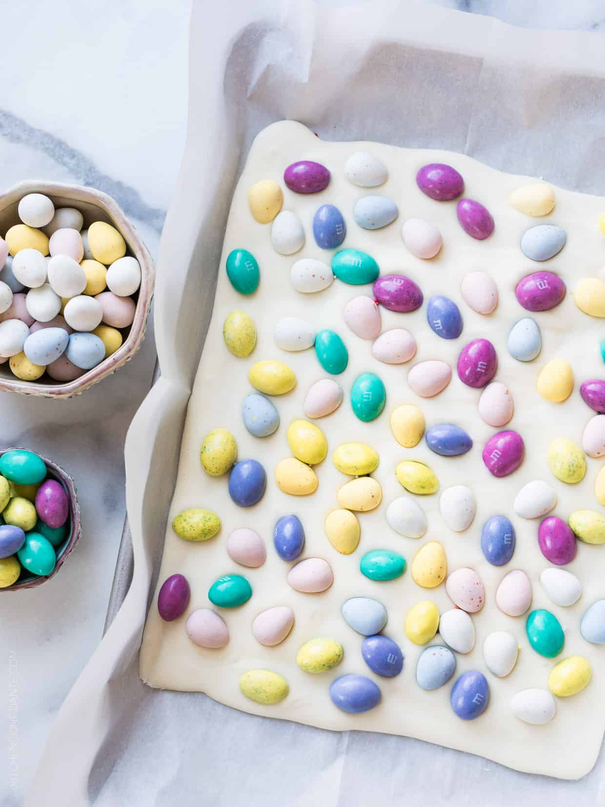 A sheet of White Chocolate Easter Bark on a baking tray surrounded by bowls of candy.