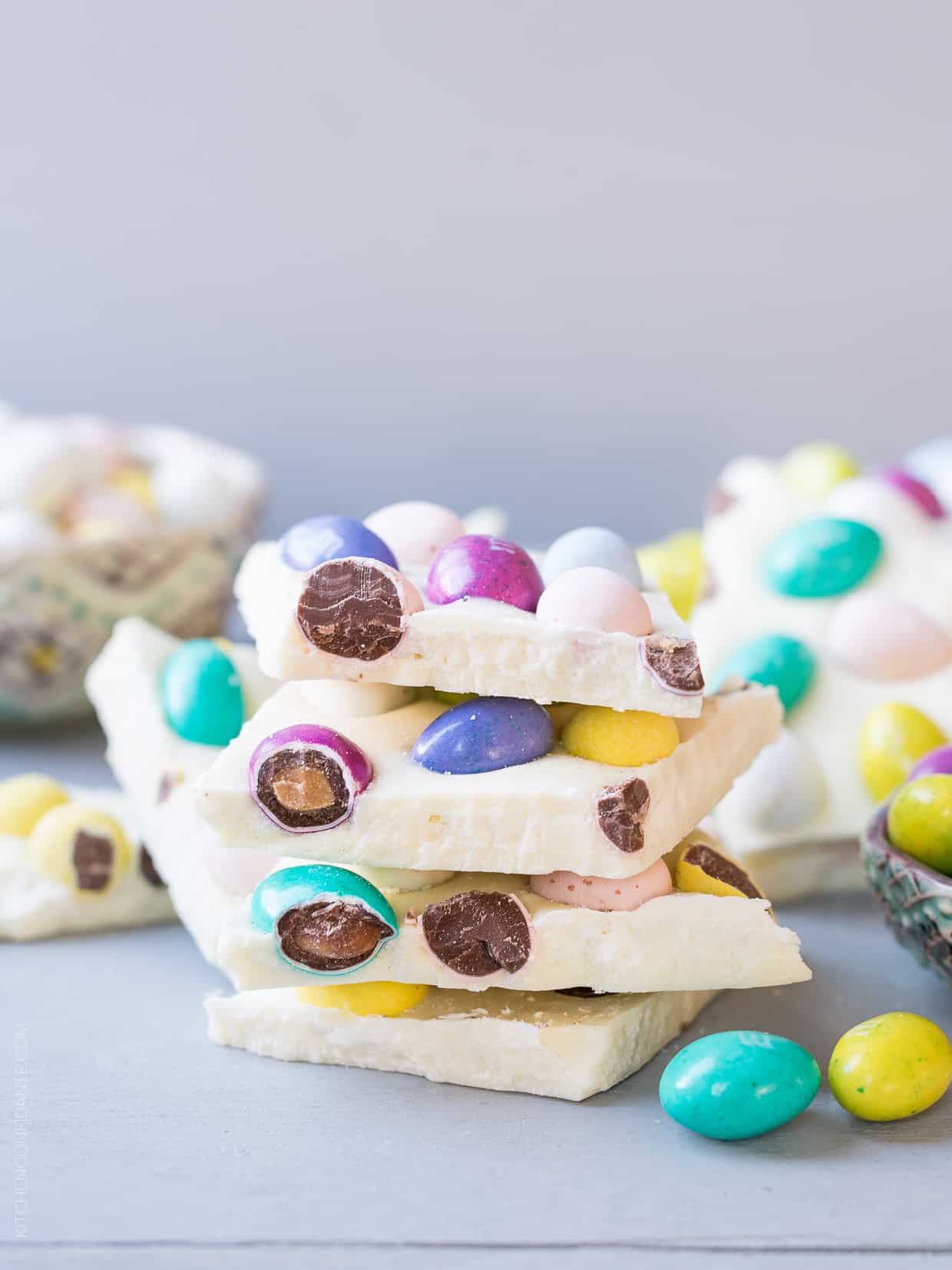 Pieces of colorful White Chocolate Easter Bark stacked on a white surface.