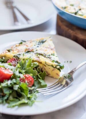 A wedge of Asparagus, Ham and Kale Frittata served on a white plate alongside a green salad.