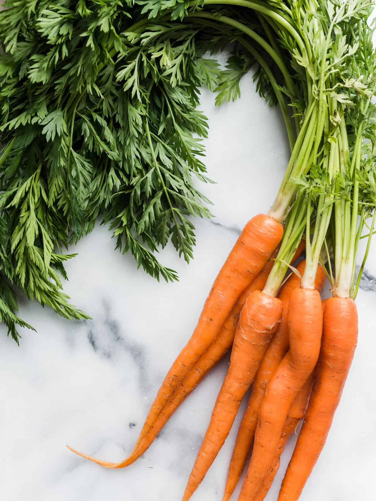 A marble surface with a bunch of fresh carrots with the tops on.