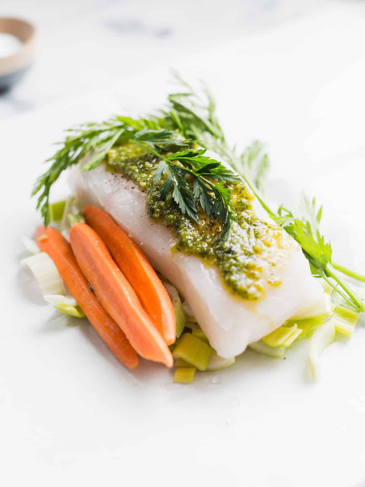 Baked halibut in parchment paper with carrot top pesto on top and carrots alongside.