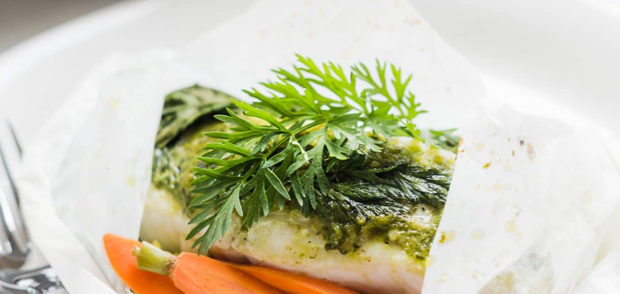 Baked halibut in parchment paper with carrot top pesto on top.