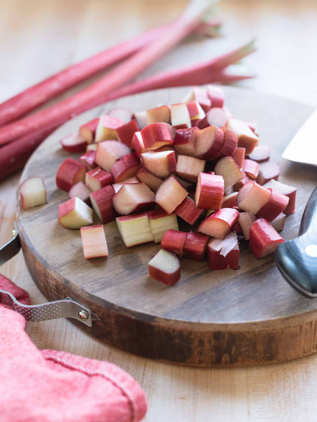 Chopped rhubarb on a wooden board with stalks of rhubarb in the background.