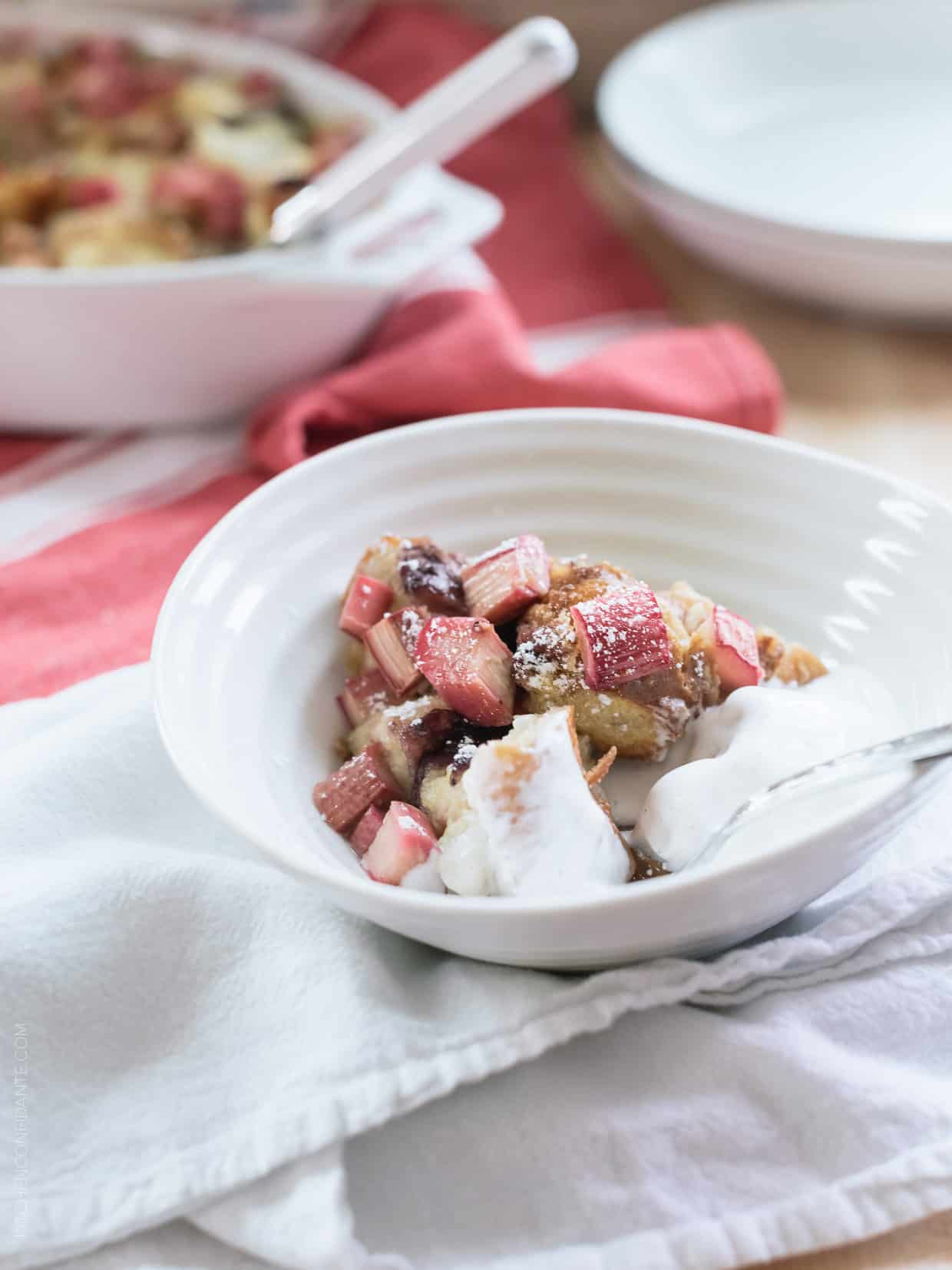 Rhubarb Bread Pudding in a white bowl topped with a scoop of vanilla ice cream.