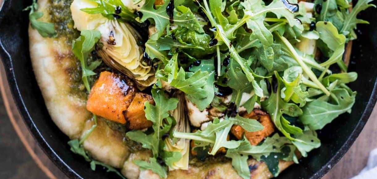 Cast iron skillet filled with Skillet Pesto Flatbread with Goat Cheese, Artichokes and Roasted Butternut Squash.