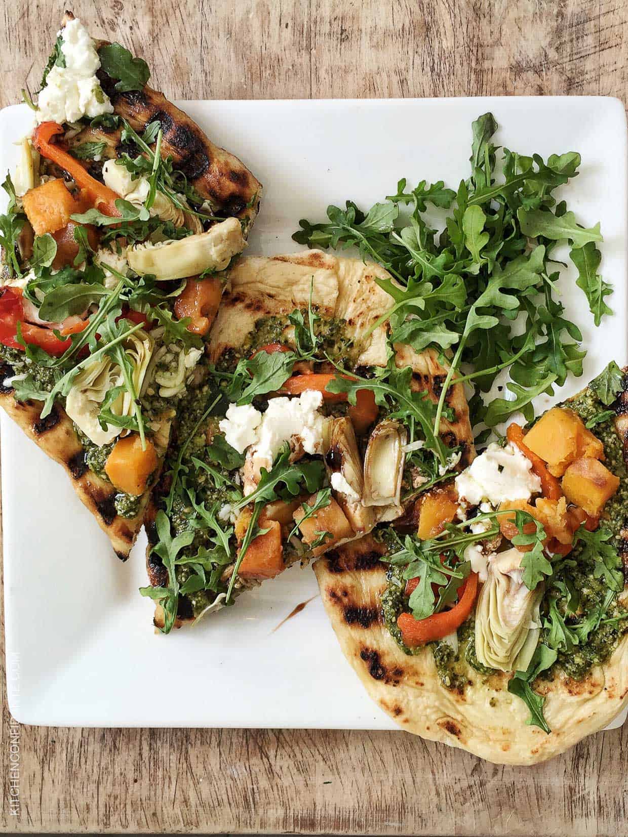 Slices of Skillet Pesto Flatbread with Goat Cheese, Artichokes and Roasted Butternut Squash on a white plate.