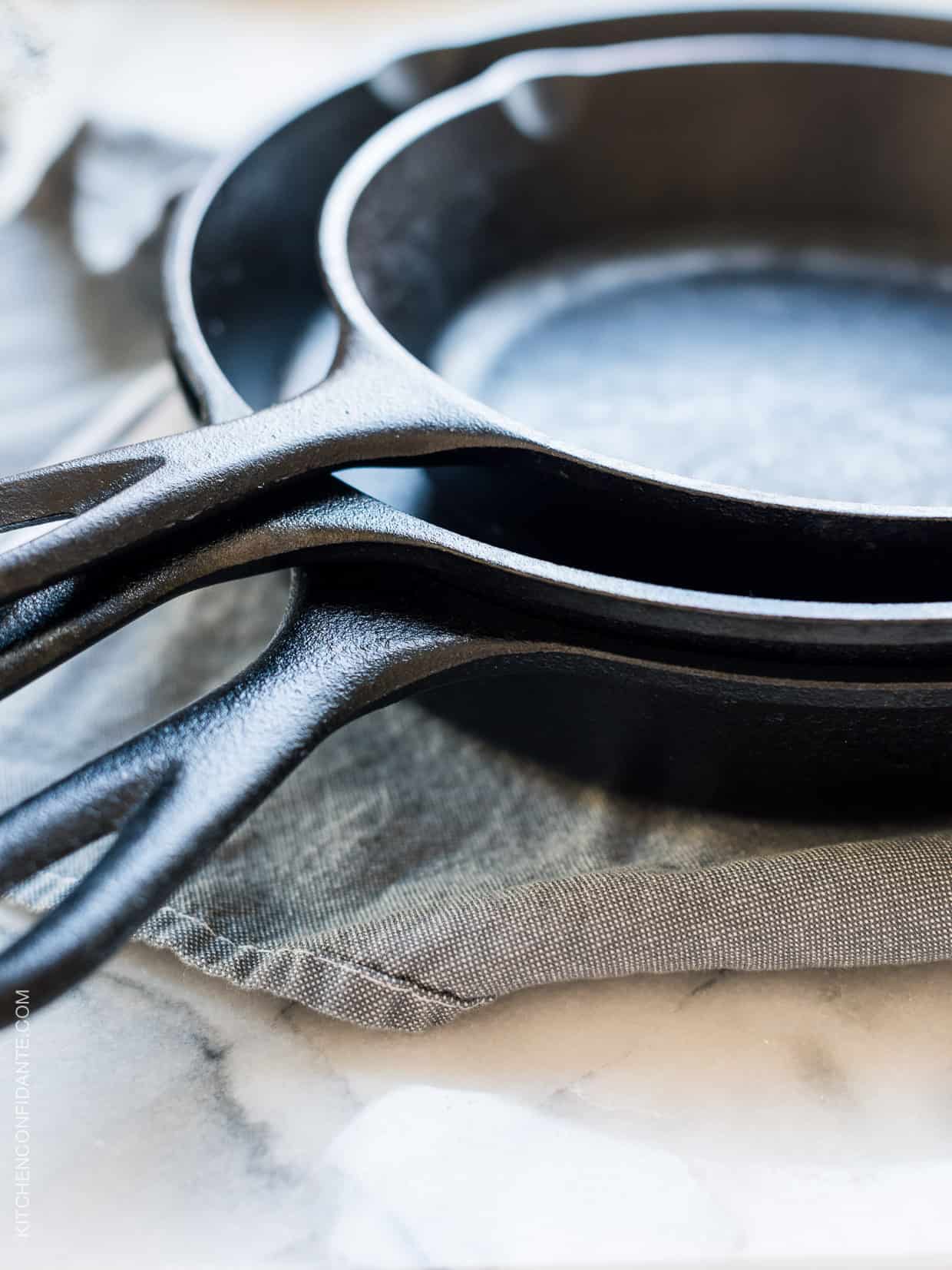 Three cast iron skillets stacked on a cloth.