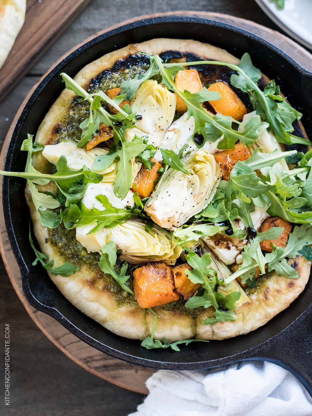 Cast iron skillet filled with Skillet Pesto Flatbread with Goat Cheese, Artichokes and Roasted Butternut Squash.