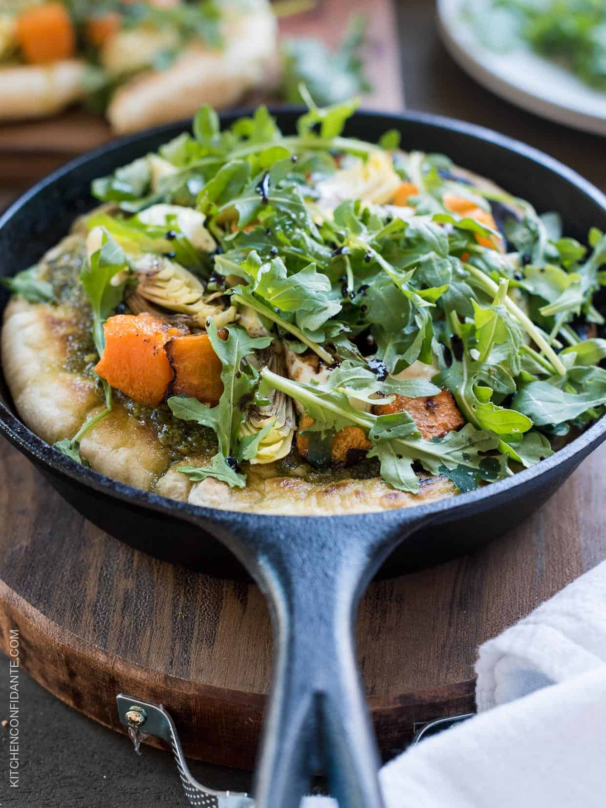 Cast iron skillet filled with Skillet Pesto Flatbread with Goat Cheese, Artichokes and Roasted Butternut Squash.
