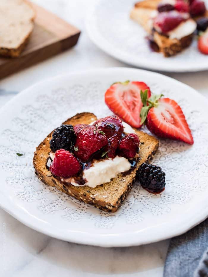 Toast topped with burrata cheese and balsamic berries on a white plate.