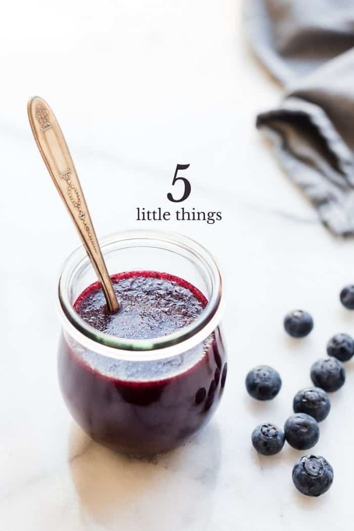 Glass jar of blueberry dressing surrounded by fresh blueberries.