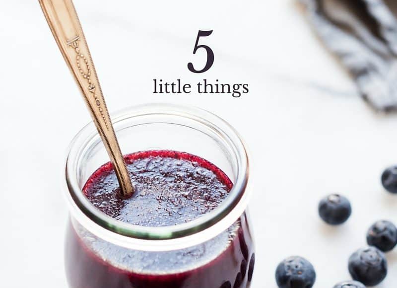 Glass jar of blueberry dressing surrounded by fresh blueberries.