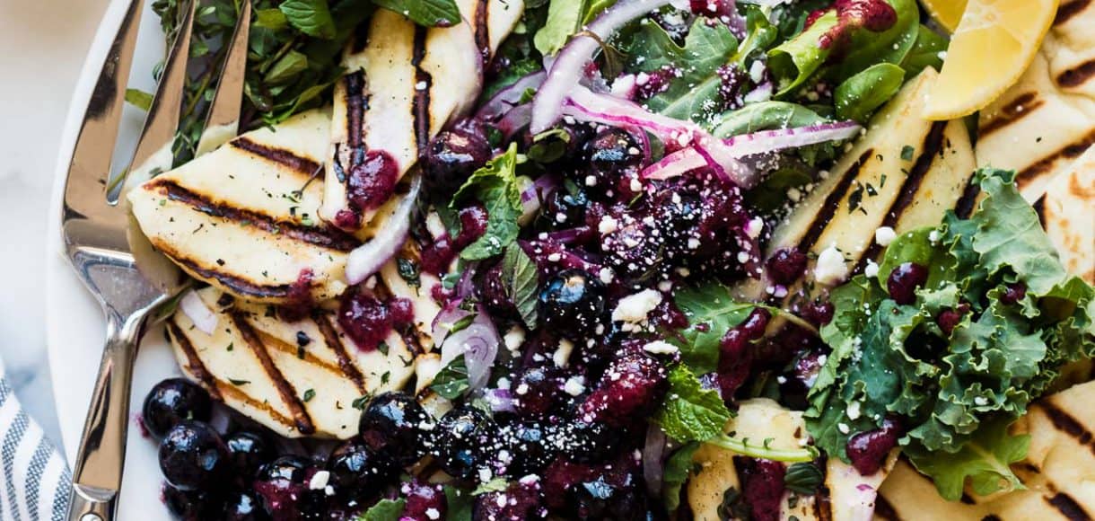 Grilled halloumi cheese served on top of a mixed green salad with a fresh blueberry dressing.