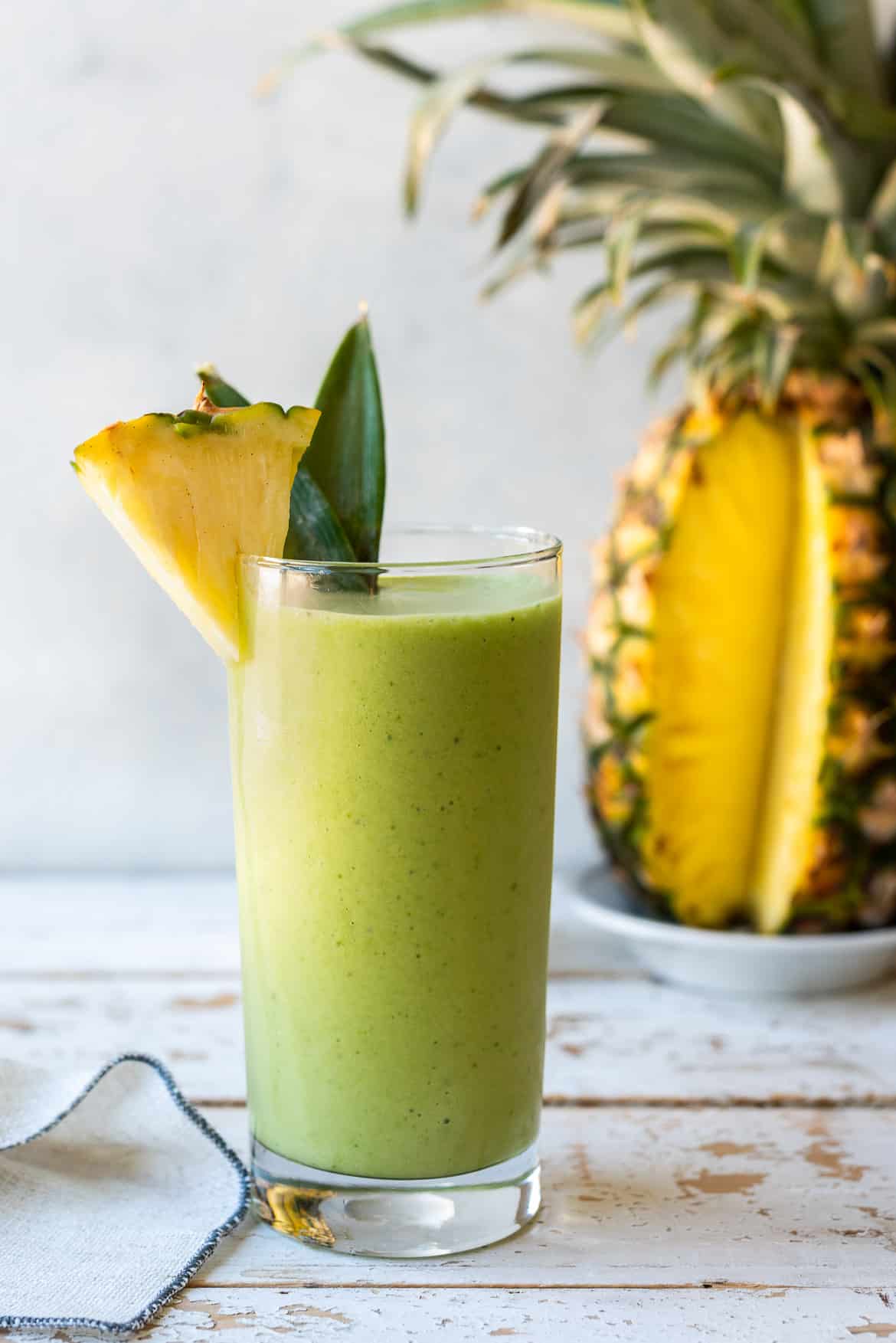 Piña Colada Green Smoothie in a tall glass garnished with fresh pineapple.