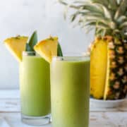 Piña Colada Green Smoothies in glasses garnished with fresh pineapple.