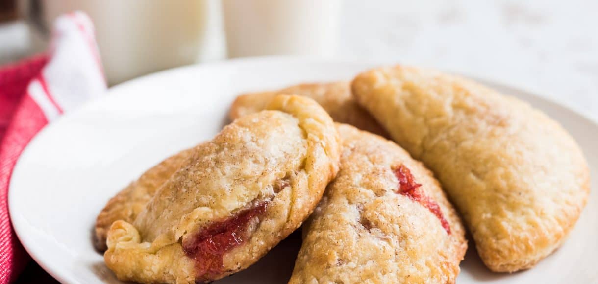 White plate with four small rhubarb empanadas on it.