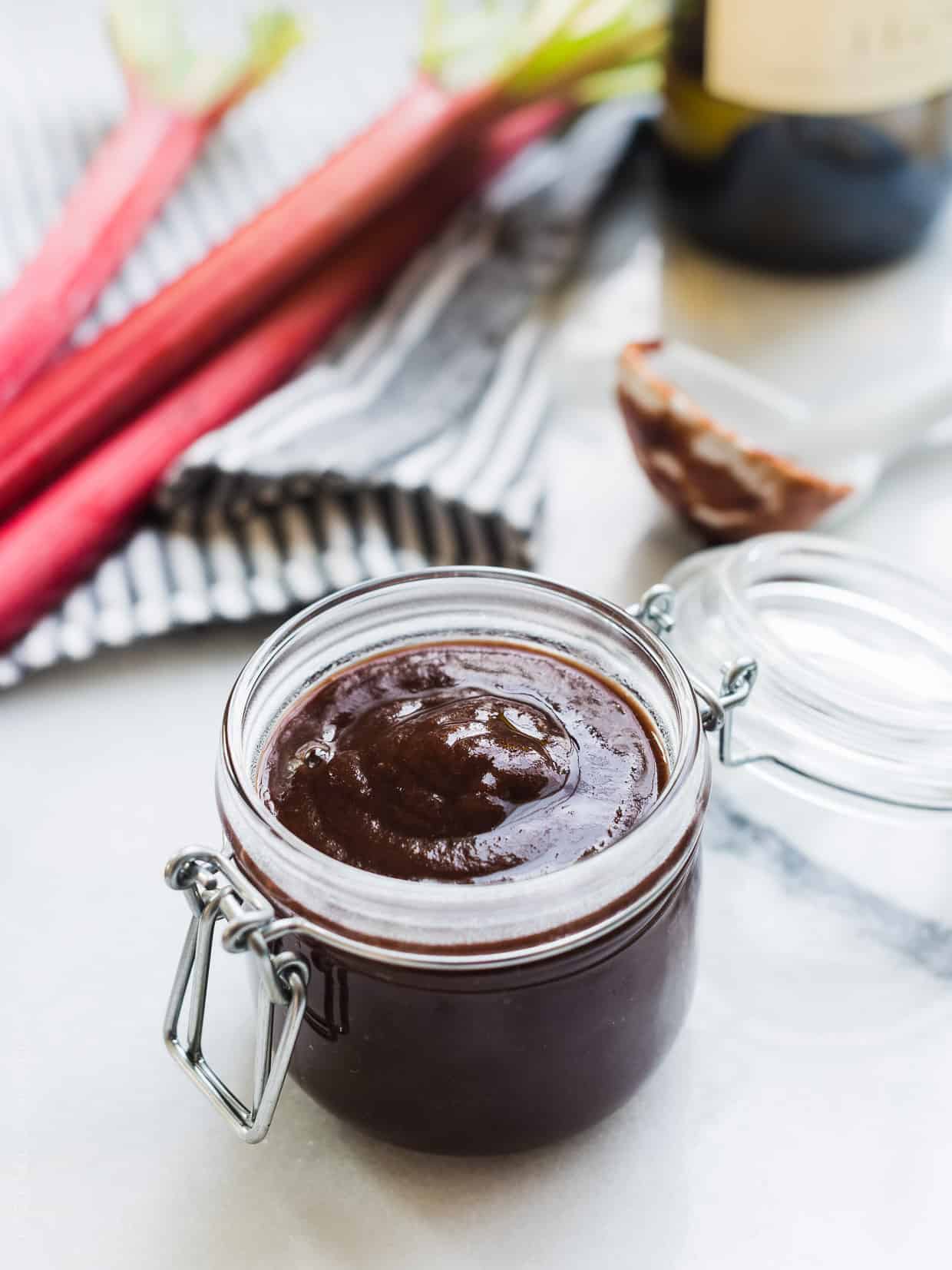 Glass jar of Rhubarb-Wine BBQ sauce surrounded by fresh stalks of rhubarb.