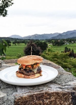 Sweet and Smoky Spanish Beef Burger on a white plate on a rock outdoors.