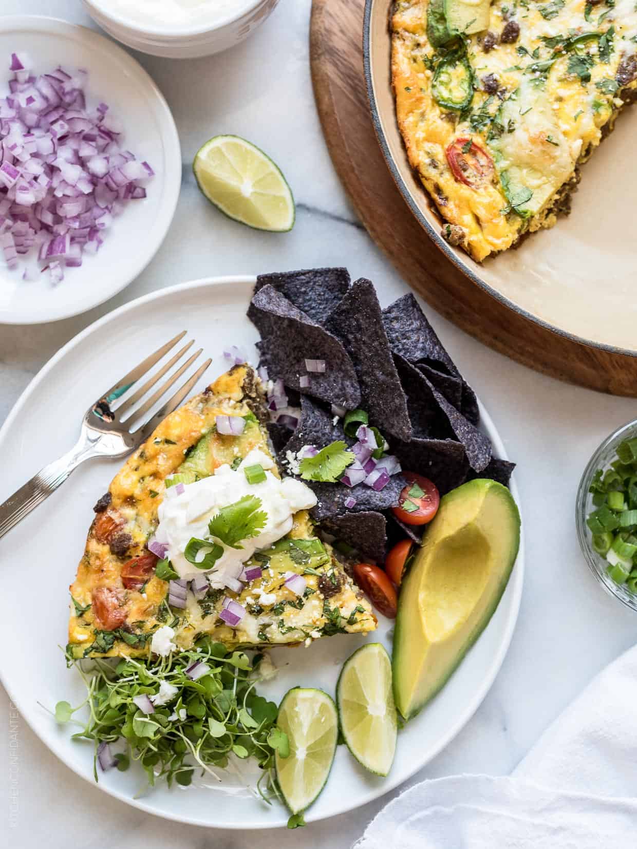 Wedge of taco frittata served with lime wedges, tortilla chips, and avocado.