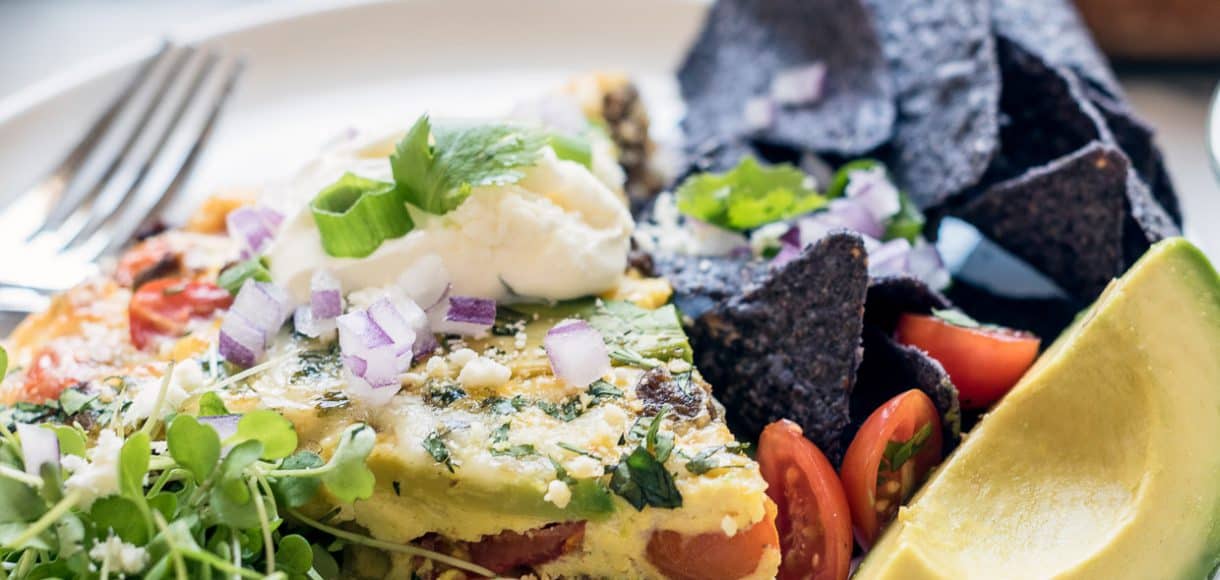 Wedge of taco frittata surrounded by a garnish of lime slices and avocado.