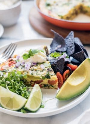 Wedge of taco frittata surrounded by a garnish of lime slices and avocado.