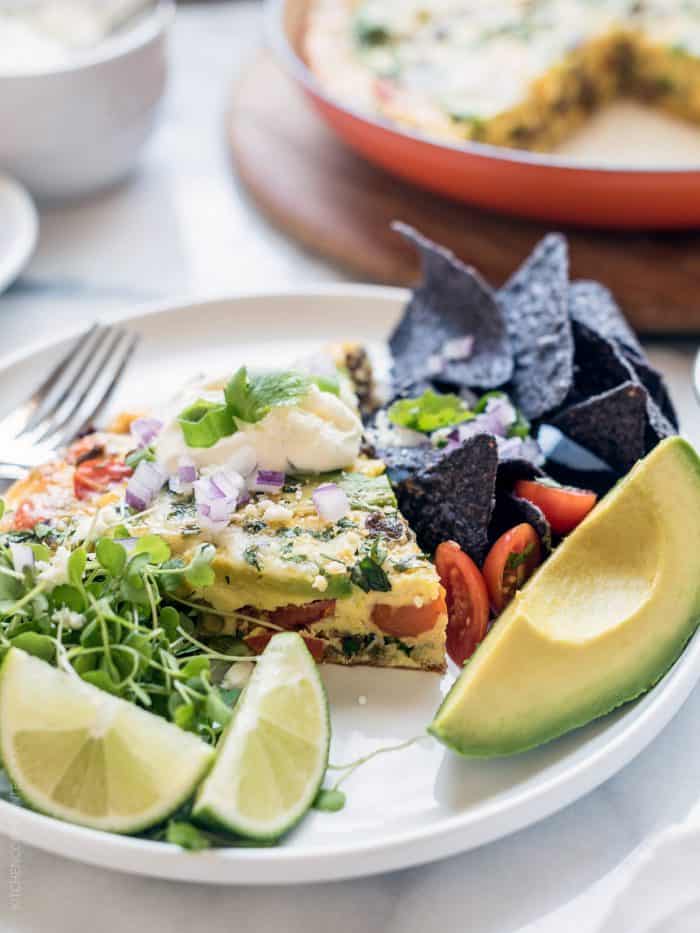 Wedge of taco frittata surrounded by a garnish of lime slices and avocado.