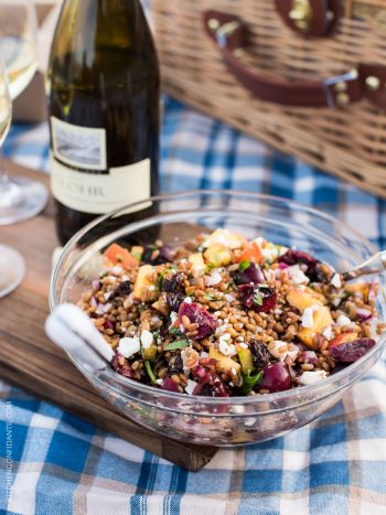 A bowl of Summer Wheat Berry Salad on a blue checkered cloth with a bottle of J. Lohr Chardonnay in the background.