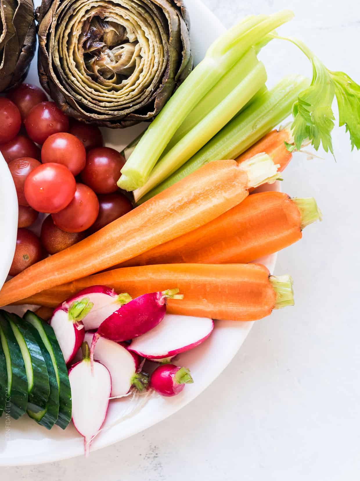 A platter of fresh vegetables including celery, tomatoes, radishes, carrots, and cucumbers.