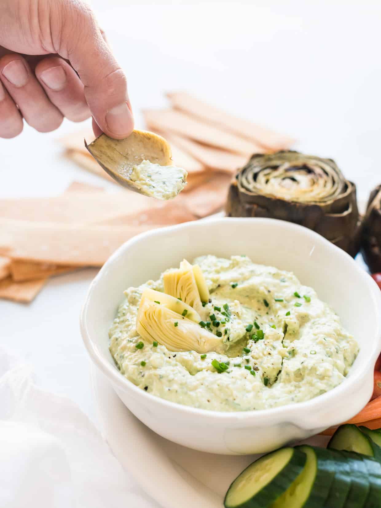 Dipping prepared artichokes into a bowl of Artichoke and Avocado Dip.