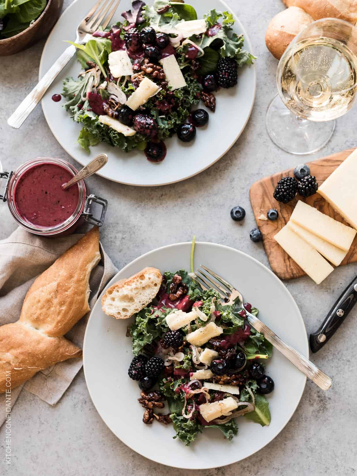 Blackberry and Blueberry Kale Salad with Aged Havarti on a white plate surrounded by sliced cheese and a baguette. 
