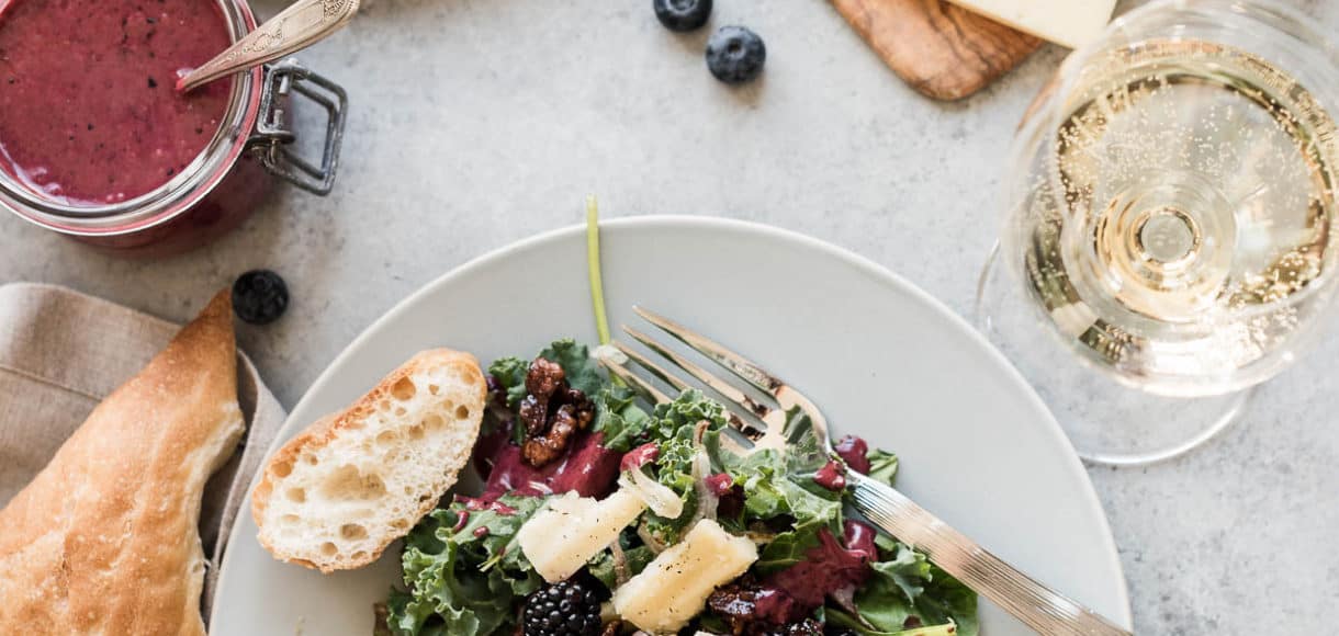 Blackberry and Blueberry Kale Salad with Aged Havarti on a white plate surrounded by sliced cheese and a baguette.