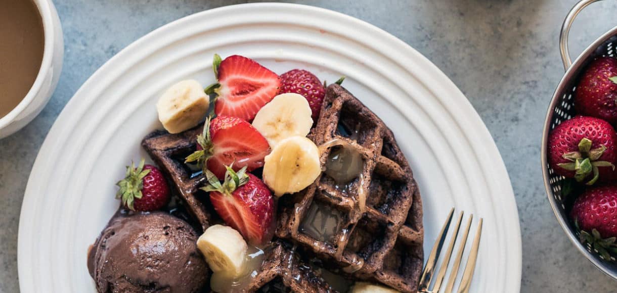 Chocolate Zucchini Belgian Waffles served on a white plate with a scoop of chocolate ice cream, syrup, and fresh fruit.