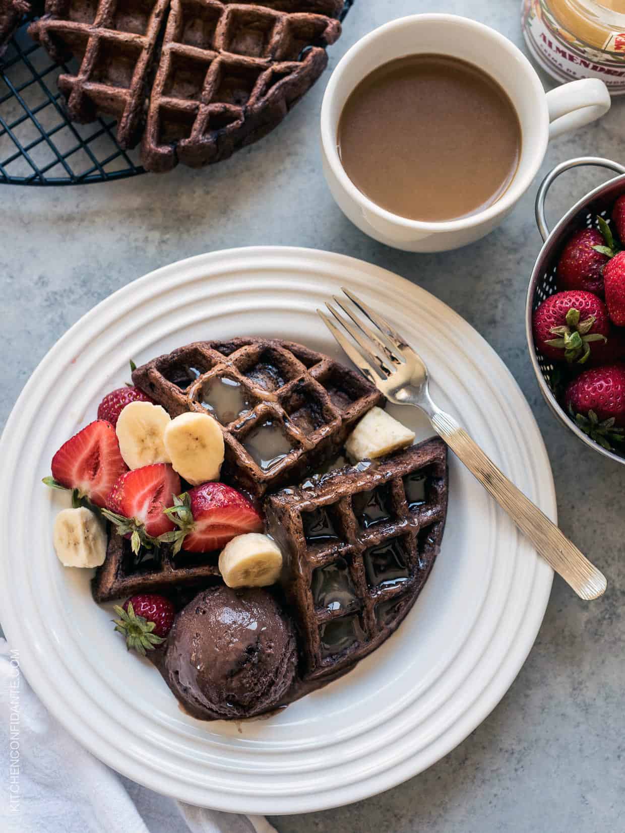 Chocolate Zucchini Belgian Waffles served on a white plate with a scoop of chocolate ice cream, syrup, and fresh fruit.