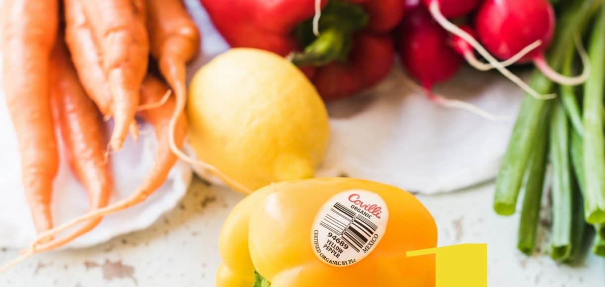 Yellow pepper with produce label surrounded by other vegetables.