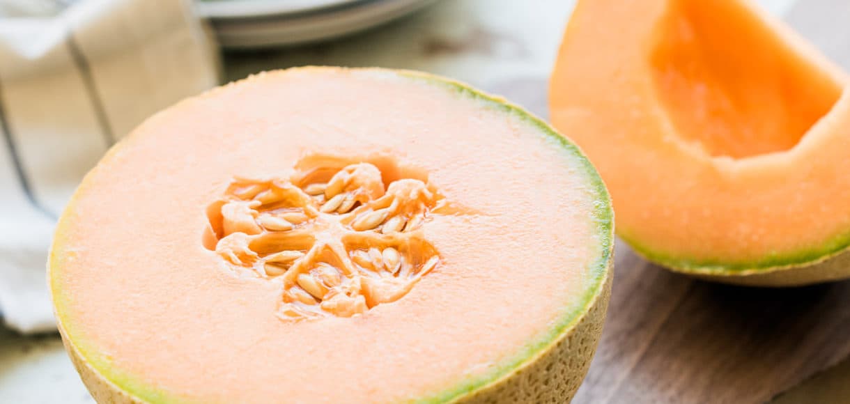Cantaloupe split in half on a wooden cutting board.