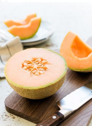 How to pick a cantaloupe -Image of a cantaloupe split in half on a wooden cutting board.