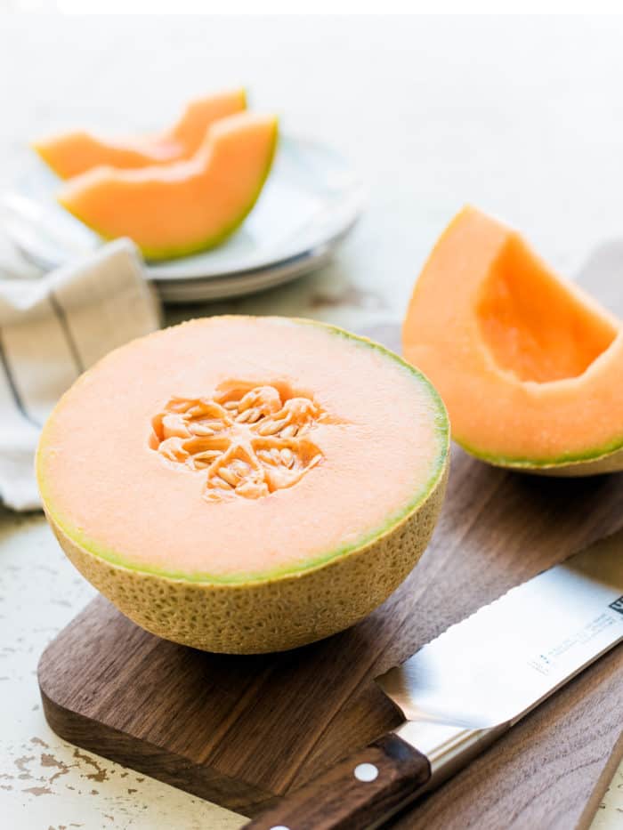 Cantaloupe split in half on a wooden cutting board.