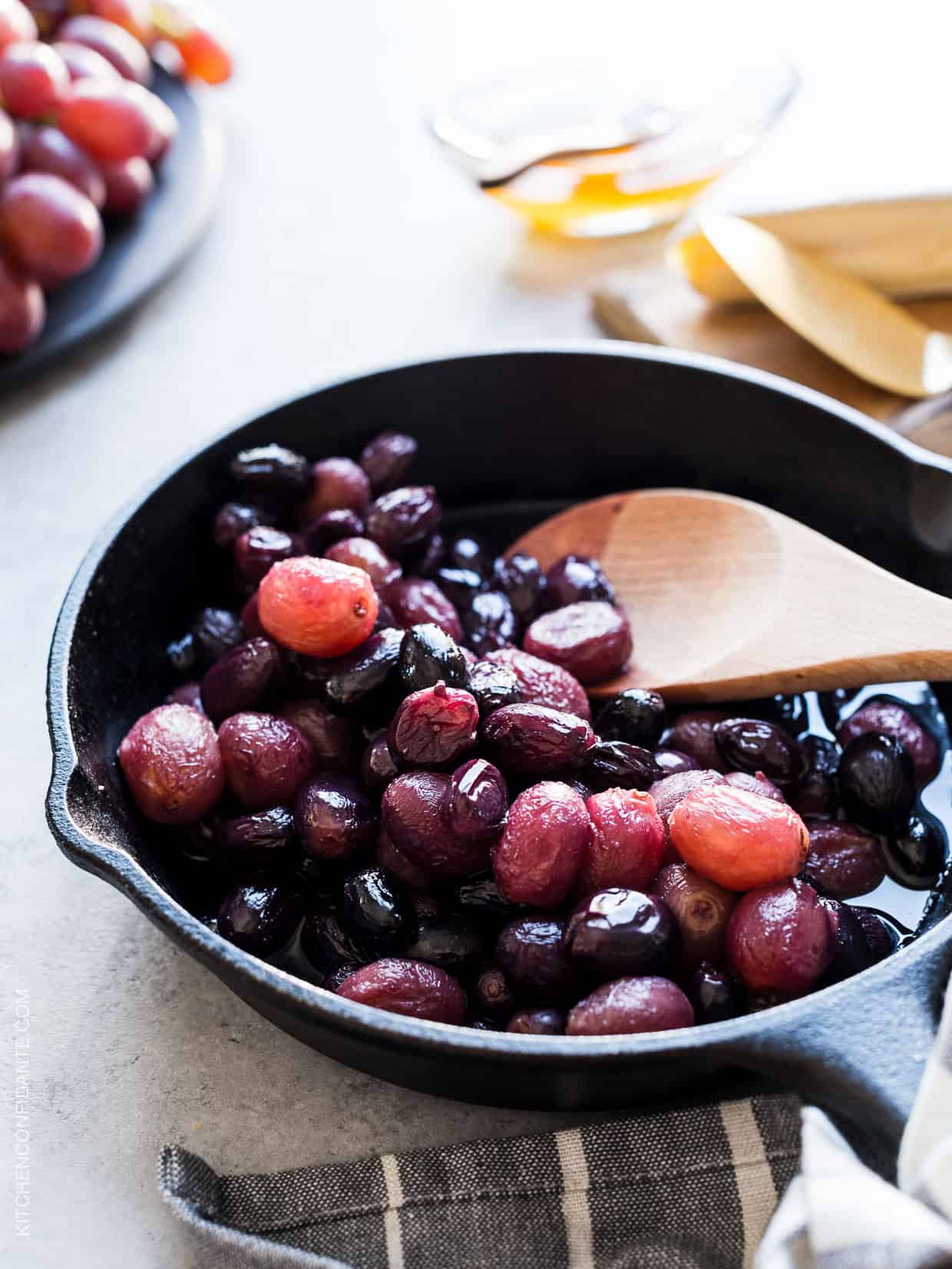 Stirring caramelized grapes with a wooden spoon in a cast iron pan.