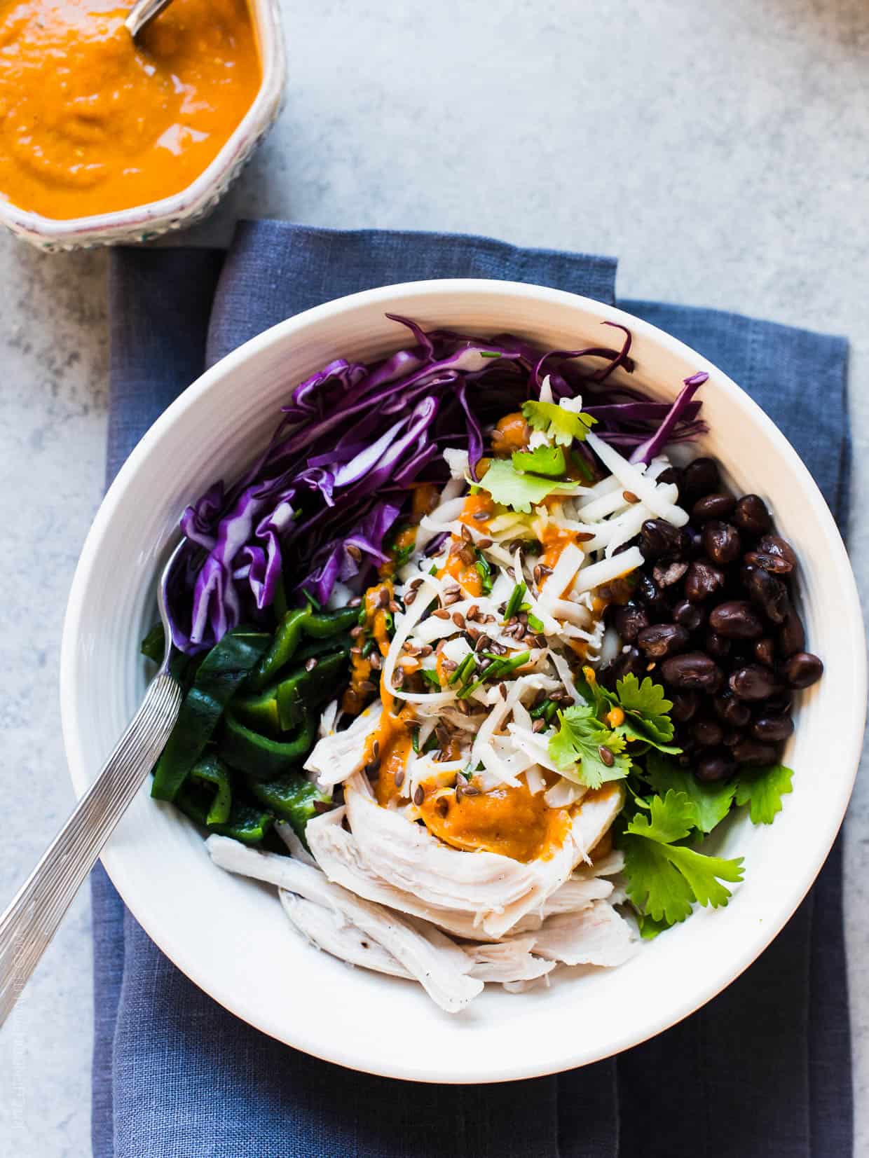 A fresh salad prepared with shredded chicken, cabbage, black beans, charred poblanos, and pumpkin-red curry vinaigrette served in a white bowl.