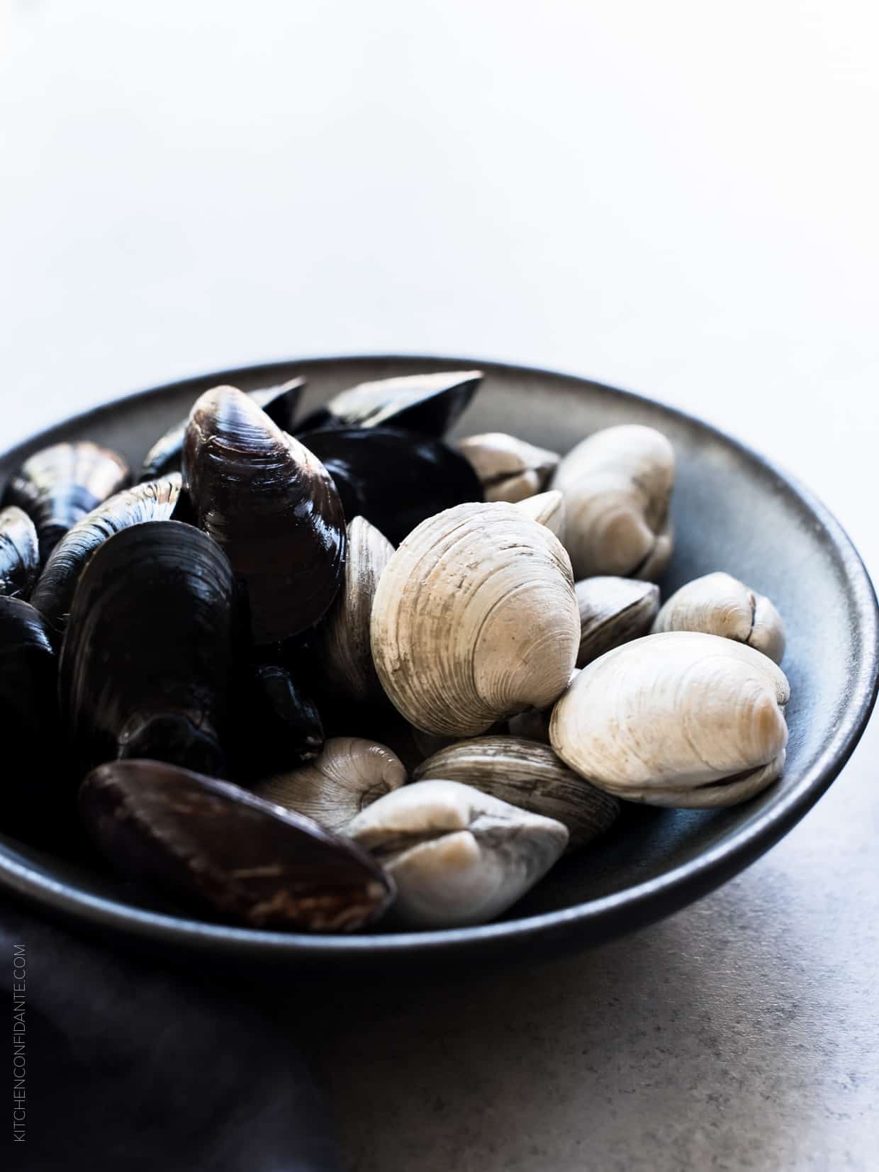 Fresh clams and mussels in a bowl on a rustic surface.