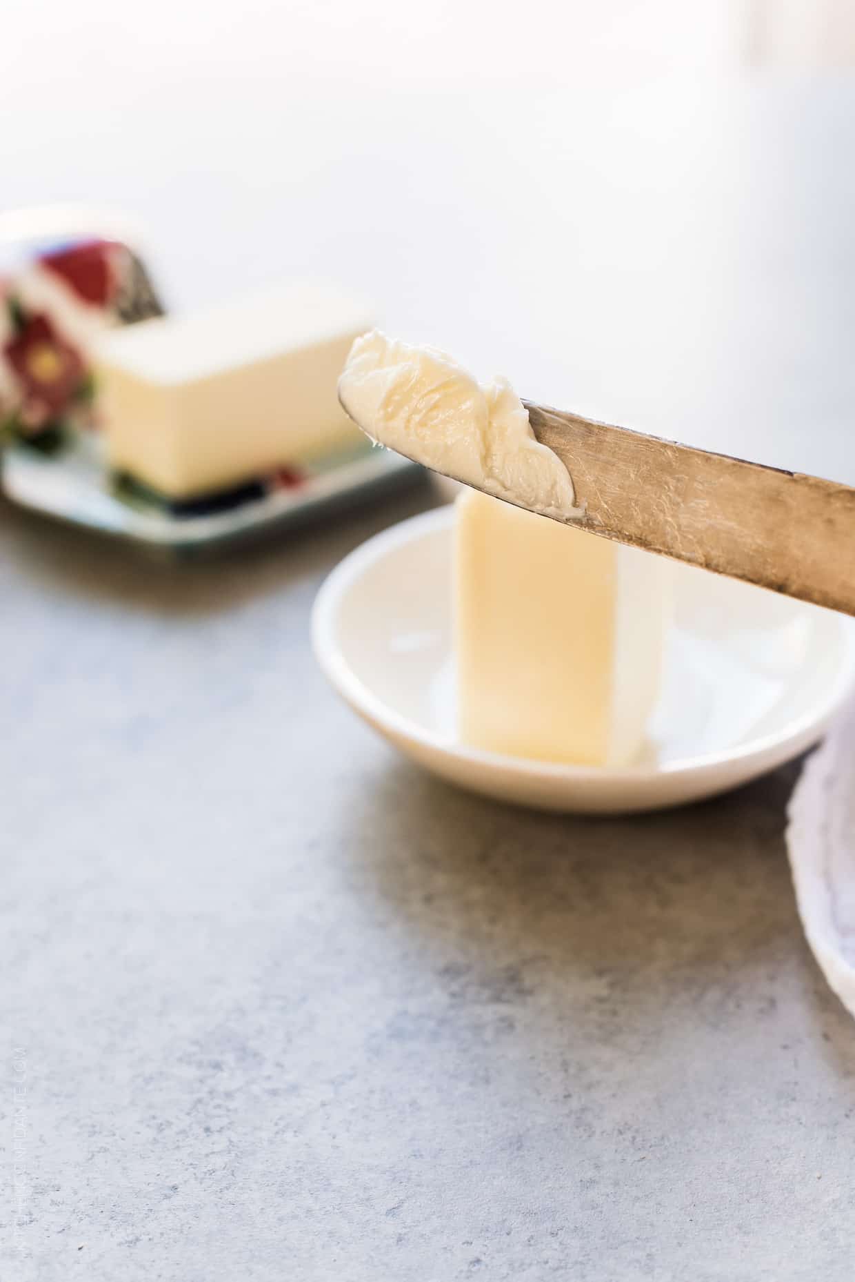 Butter knife with softened butter on it and a stick of butter in the background.
