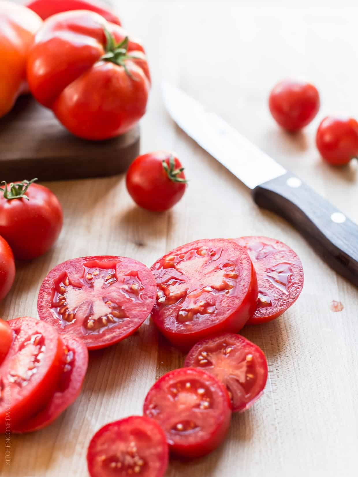 Slices of fresh heirloom tomatoes surrounded by whole tomatoes.