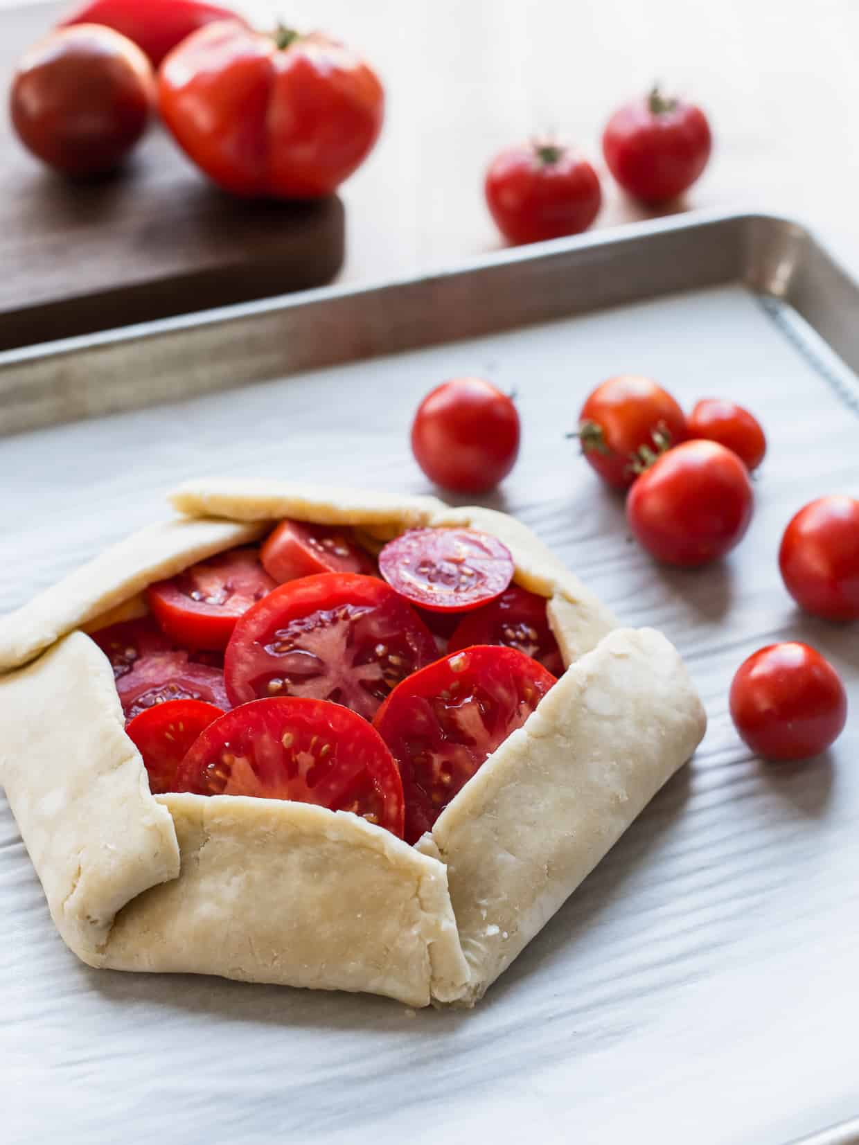 A flaky crust folded around slices of heirloom tomatoes on a baking sheet ready for the oven.