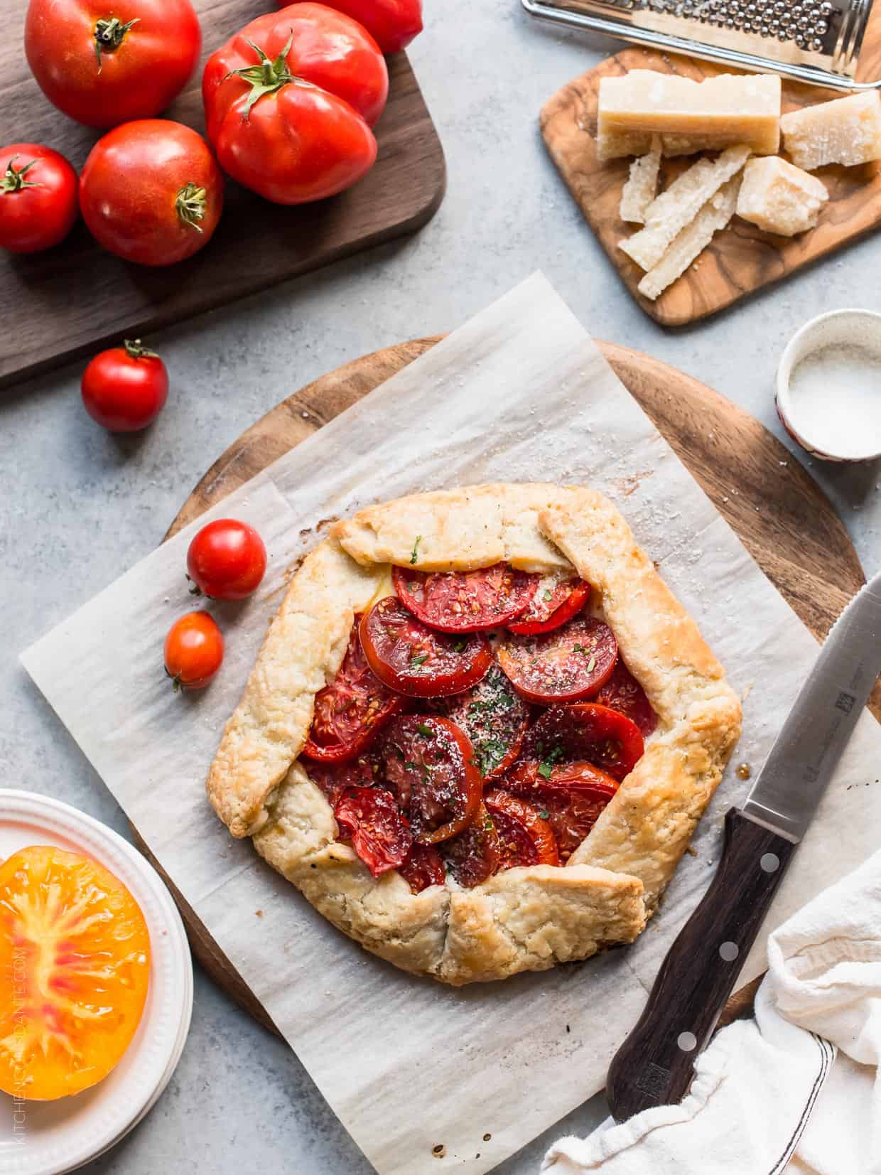 Tomato Galette surrounded by fresh heirloom tomatoes and Parmesan cheese.