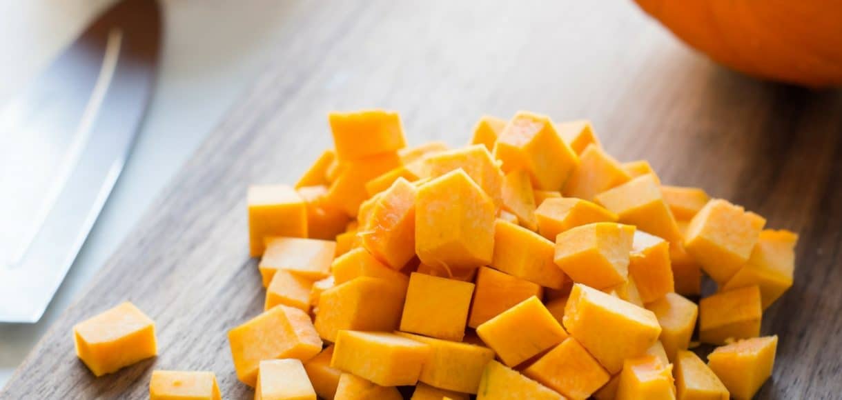 Diced fresh pumpkin on a wooden cutting board.