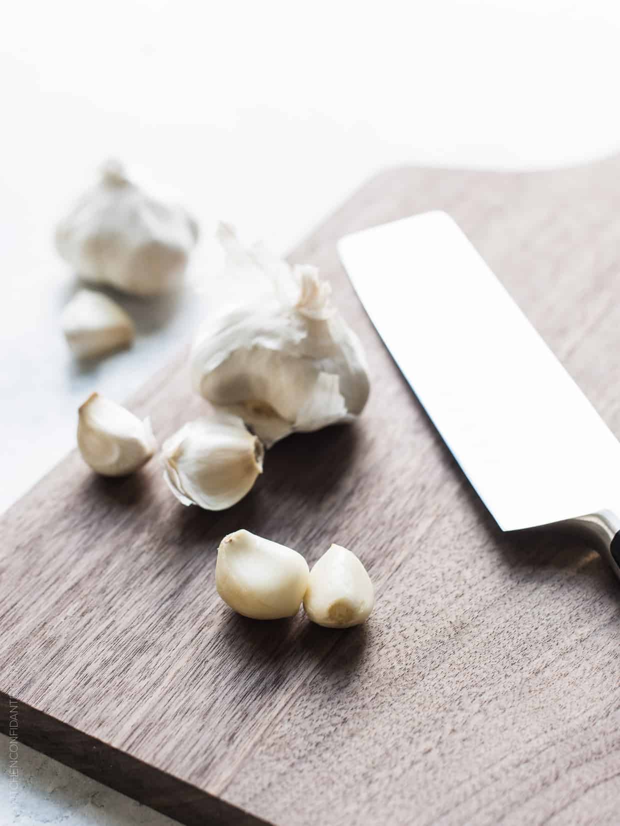 Fresh garlic cloves on a wooden cutting board with a chef's knife.